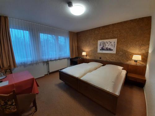 Schlafzimmer mit einem großen Bett, einem Tisch und Fenstern in der Unterkunft Hotel-Garni Pfeffermühle in Emmerthal