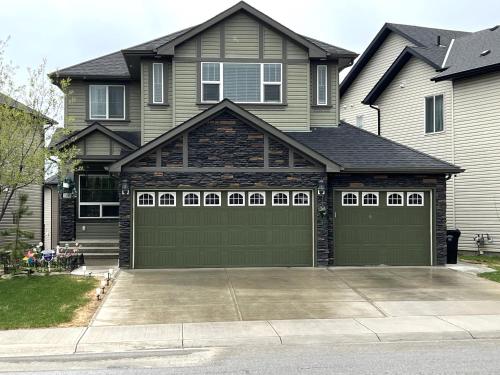 a house with green garage doors in a driveway at Luxury 4 Bedroom Cozy Home close to YYC, Shops, DT, Stampede, Mountains and many amenities in Panorama Hills NW Calgary in Calgary