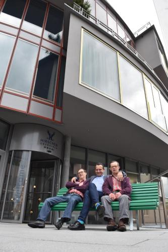 trois hommes assis sur un banc devant un bâtiment dans l'établissement HIRSCHEN OBERKIRCH - Design Boutique Hotel, à Oberkirch