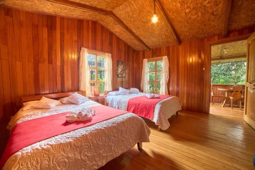 two beds in a room with wooden walls and wooden floors at Carolina Egg Gasthaus in Oxapampa