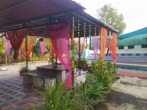 a pavilion with pink and orange curtains and plants at Kimaya farm house in Panvel