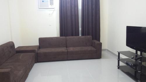 a living room with a couch and a tv at Golden Seasons Furnished Apartment in Salalah