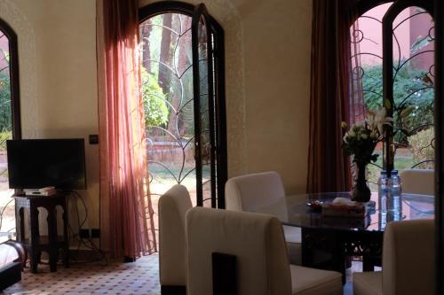Eden Palm Resident Palmeraie Marrakech في مراكش: غرفة معيشة مع طاولة وكراسي ونوافذ