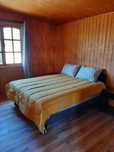 a bed in a room with a wooden wall at Cabañas de Campo MARBAJA in Puerto Montt