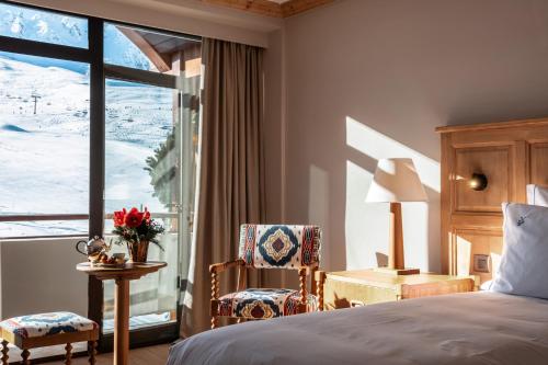 a bedroom with a bed and a chair and a window at Alpes Hôtel du Pralong in Courchevel