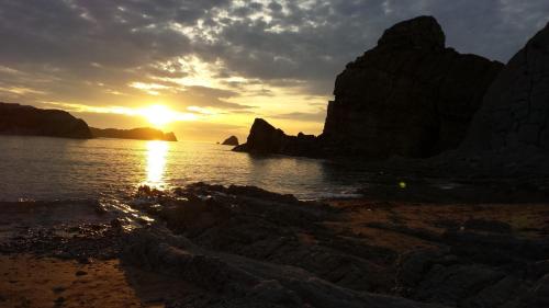 a sunset on a beach with rocks in the water at Hostal la Picota in Liencres