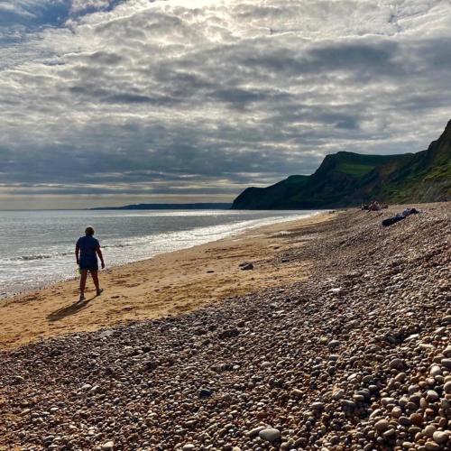 a man walking on a beach near the water at Strongate View Apartment - cosy stylish rural Jurassic coast & Bridport nearby in Netherbury