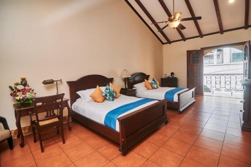 a bedroom with two beds and a table and a desk at Hotel Plaza Colon - Granada Nicaragua in Granada