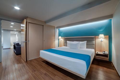1 dormitorio con 1 cama grande y pared azul en City Express Suites by Marriott Anzures, en Ciudad de México
