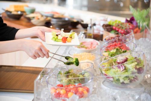 a person holding a plate of food on a table at Richmond Hotel Utsunomiya-ekimae Annex in Utsunomiya