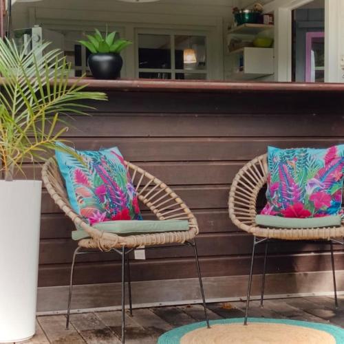 two wicker chairs with colorful pillows on a porch at Cabane intime Nid’Amour, Jacuzzi privé in La Plaine