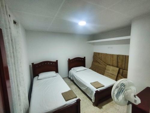 Duas camas num pequeno quarto com uma ventoinha. em Hostal, casa Jaramillo em Roldanillo