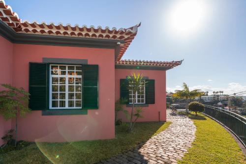 a pink house with green windows and a train at Casa Coelho in Ponta do Sol
