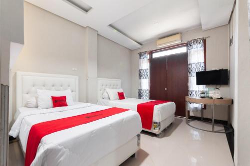 two beds in a white room with a television at RedDoorz Syariah near Pasar Aceh Shopping Centre in Banda Aceh