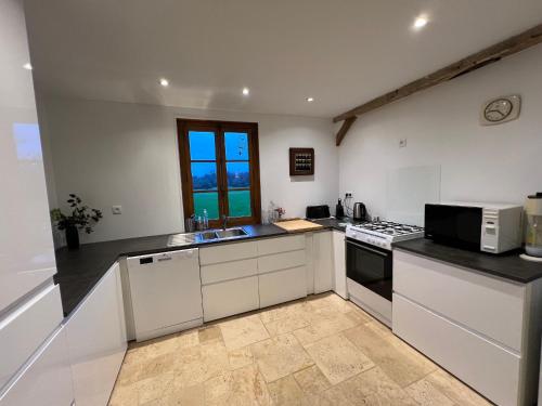 une cuisine avec des armoires blanches et un four à plaques de cuisson dans l'établissement Évasion en Sologne : Gîte PMR, Billard, Tennis & Nature Proche Châteaux de la Loire - FR-1-590-420, à Jouy-le-Potier