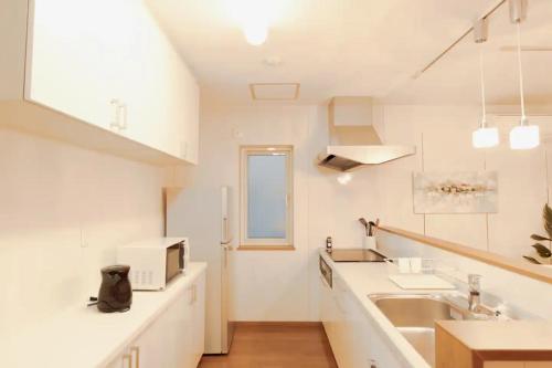 cocina con armarios blancos, fregadero y encimera en ファミリア・デザインハウス札幌, en Sapporo