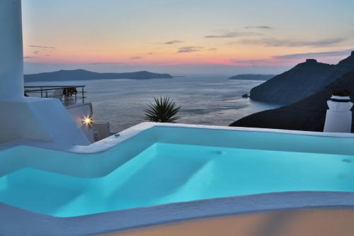 a swimming pool with a view of the ocean at sunset at Trieris Villa & Suites in Fira
