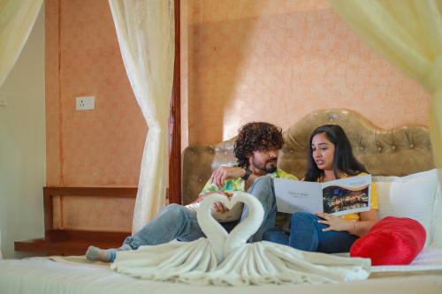 two people sitting on a bed reading a book at Kuruva Island Resort And Spa - By KABINI BREEZE in Mananthavady