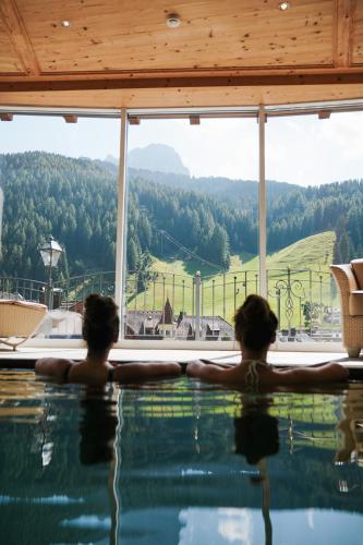 two people standing in a swimming pool looking out a window at Hotel Sun Valley in Selva di Val Gardena