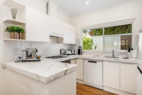 a white kitchen with white cabinets and a window at Swainson on Penzance in Glenelg