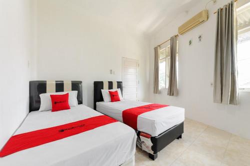 two beds in a room with white walls and red pillows at RedDoorz Syariah near Suzuya Mall Banda Aceh in Banda Aceh