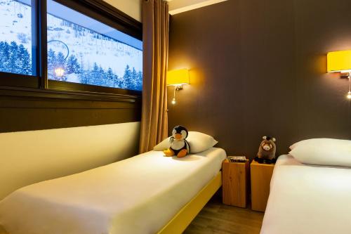 a room with two beds and a window with a stuffed animal on the pillow at SOWELL RESIDENCES Pierre Blanche in Les Menuires