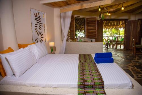 a bedroom with a large white bed with two blue chairs at Bottle Cottage in Shimoni