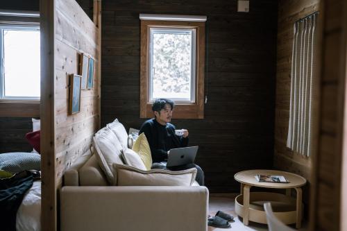 a man sitting on a couch with a laptop at 美瑛森林木屋 - 小紅帽 in Biei
