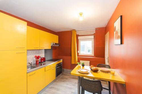 una cocina con armarios naranjas y amarillos y una mesa. en LE RED LINE I NETFLIX I BILLARD I WIFI I PARKING I CENTRE-VILLE - Cosy & Confort, en Valenciennes