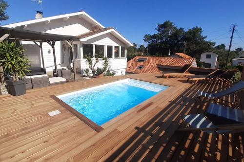 une terrasse en bois avec une piscine et une maison dans l'établissement Villa les Roses, à Capbreton