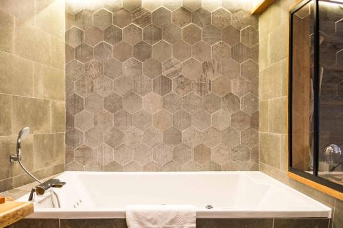 a bathroom with a white tub and a tile wall at Les Jardins d'Epicure in Bray-et-Lû