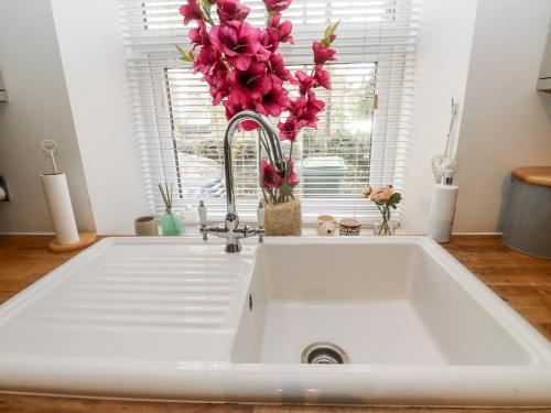 a kitchen sink with pink flowers in a window at The Cottage in Yeadon