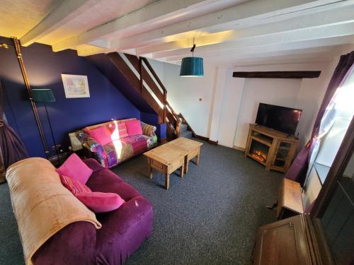ein Wohnzimmer mit einem lila Sofa und einem TV in der Unterkunft Charming pet friendly 2 bedroom cottage, close to Narberth & local beaches, friendly animals on our smallholding in Pembrokeshire