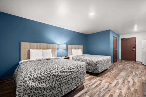 two beds in a room with blue walls and wooden floors at WoodSpring Suites Dearborn Detroit in Dearborn