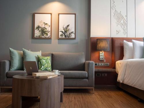 a hotel room with a couch and a bed at Novotel Living Bangkok Sukhumvit Legacy in Bangkok