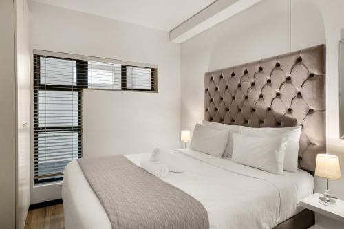 a white bedroom with a large bed and a window at Easy Stay - The Vantage Rosebank in Johannesburg