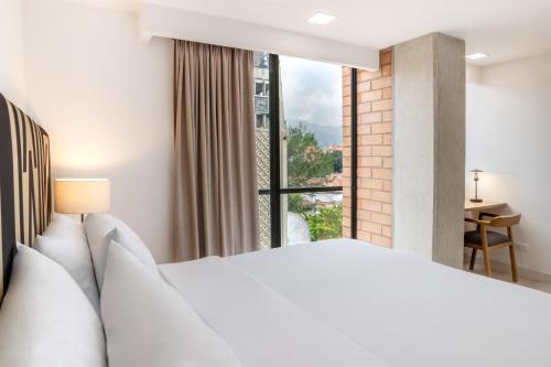 a bedroom with a white bed and a large window at Origen Local Suites in Medellín