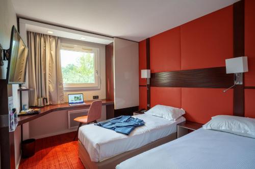 a hotel room with two beds and a desk and a window at Kyriad Nantes Sud - Bouaye Aéroport in Bouaye
