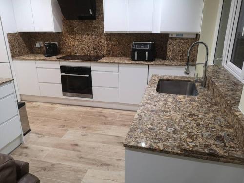 cocina con armarios blancos y encimera de granito en NightRest Homes 5 Bedroom House - Smart Tv in Each Room-Parking-Wifi en Welwyn Garden City