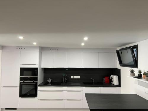 une cuisine blanche avec des appareils noirs et une télévision dans l'établissement Logement design entier neuf à Paris Gentilly, à Gentilly