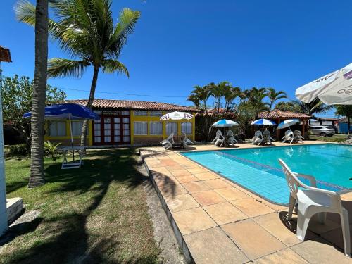 プラドにあるRecanto dos Passárosの椅子とパラソルとヤシの木のあるプール