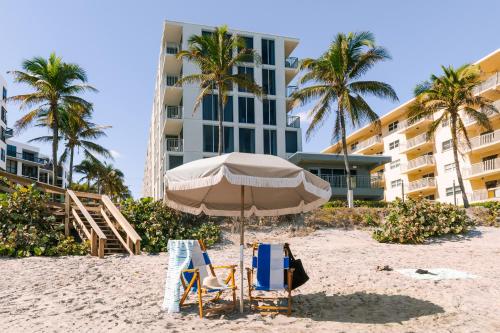 a beach with two chairs and an umbrella and a building at The Hillsboro powered by Sonder in Deerfield Beach