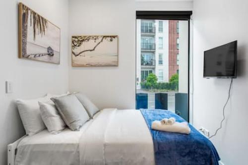 een witte slaapkamer met een bed en een televisie bij Urban Thrive Studio is in a great location in Auckland
