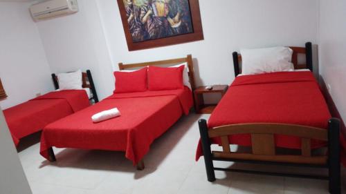 1 dormitorio con 2 camas con sábanas rojas y silla en Hotel La Casona Vieja, en Valledupar