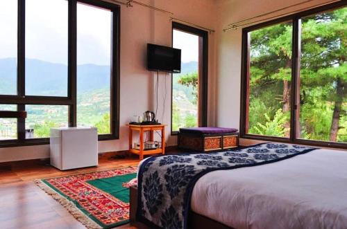 a bedroom with large windows with a bed and a television at Himalayan Star Resort in Paro