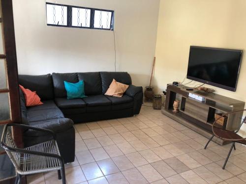 a living room with a black couch and a flat screen tv at Casa grande com churrasqueira - Centro Ubatuba in Ubatuba