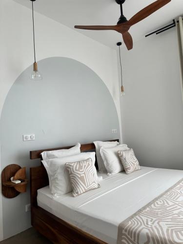 a bed with white pillows and a ceiling fan at PASSOT HILLS in Nosy Be