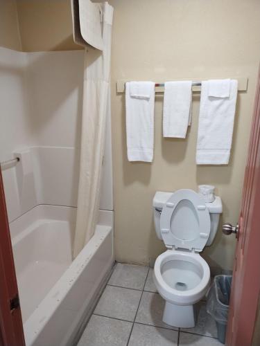a bathroom with a toilet and a tub and towels at Howards Inn Motel in Eunice