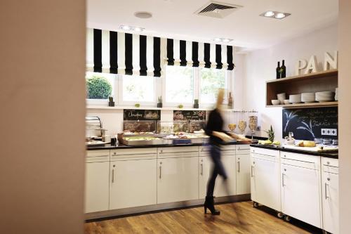 a person walking in a kitchen with white cabinets at Hotel Bonjour in Bad Soden am Taunus