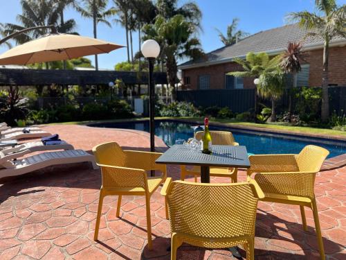 un patio con mesa, sillas y piscina en Coastal Waters Motor Inn, en Lakes Entrance